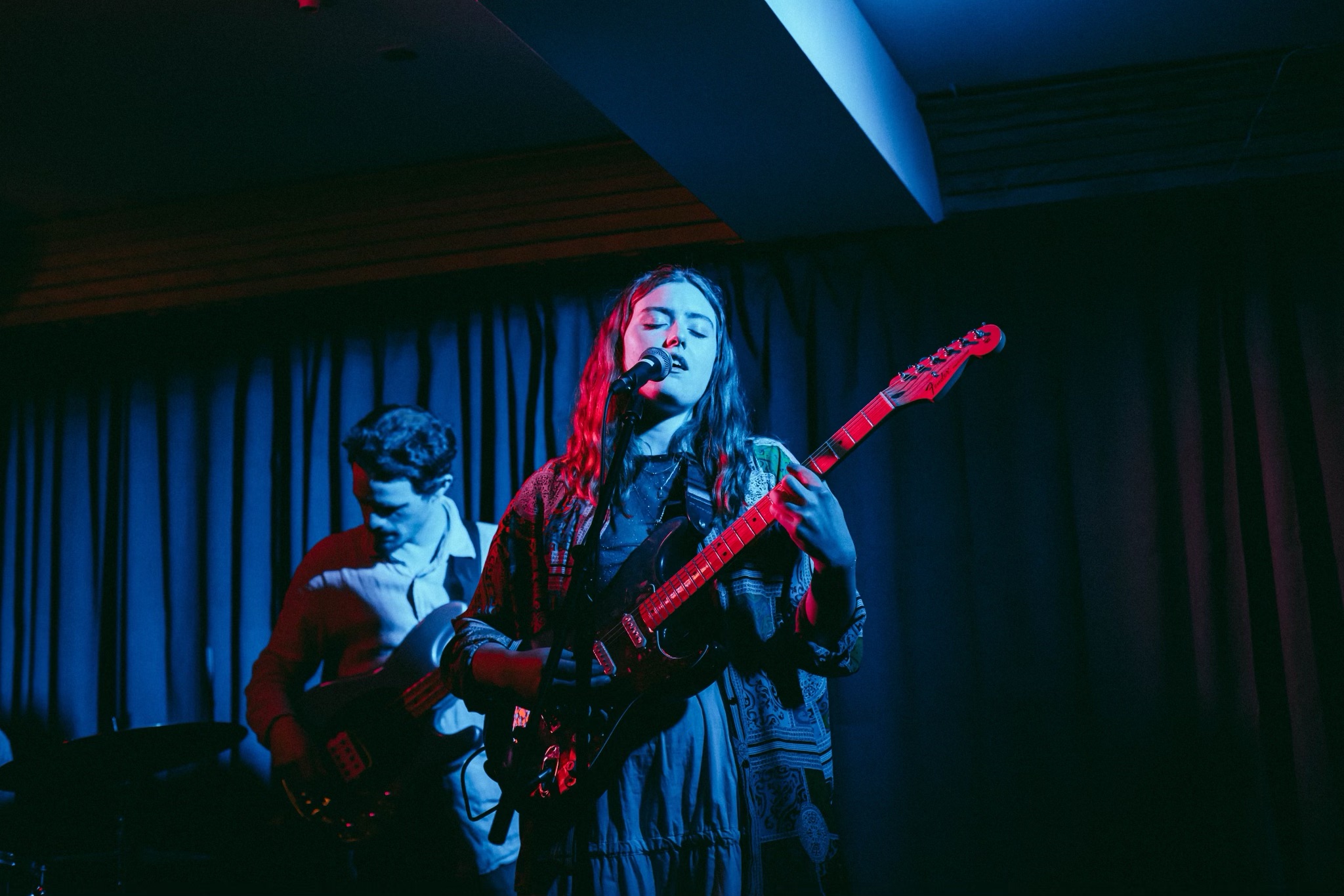 Image of Jackie Marchal playing her guitar on a dramatically blue and pink lit stage