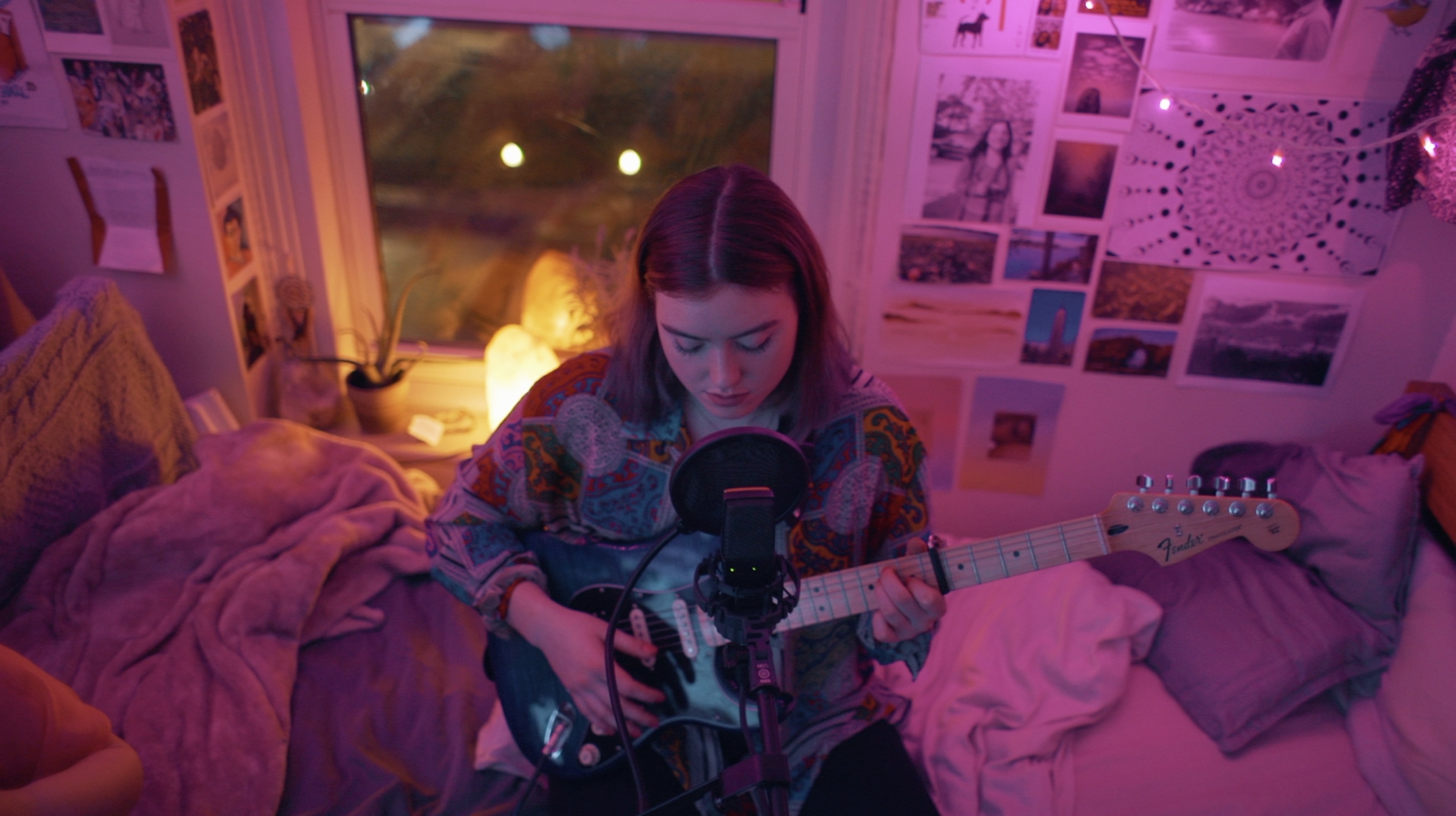 Image of Jackie Marchal playing her guitar in a cozy pink-lit room.